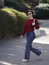 A lady wears a red cardigan and bootcut jeans.